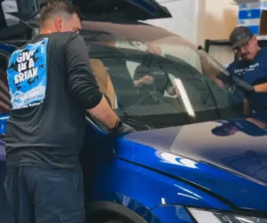 Technician Installing Windshield at Clear Cut Glass and Tint Clear Cut Glass and Tint technician installing a windshield on a blue vehicle inside the shop