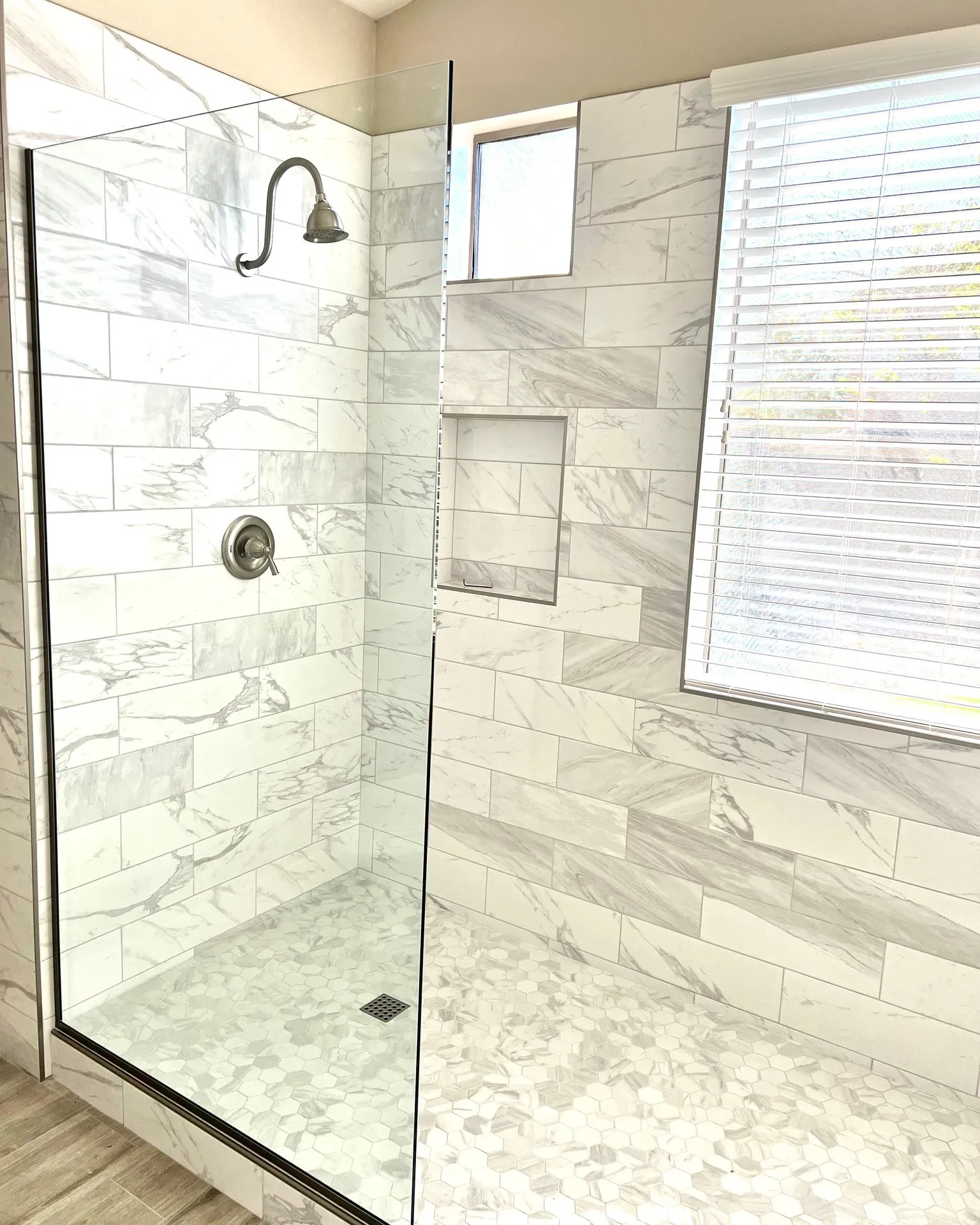 Frameless Fixed Glass Shower with Window and Niche | Clear Cut Glass and Tint Frameless fixed glass shower panel with marble-look tile, built-in niche, and bathroom window installed by Clear Cut Glass and Tint in Arizona
