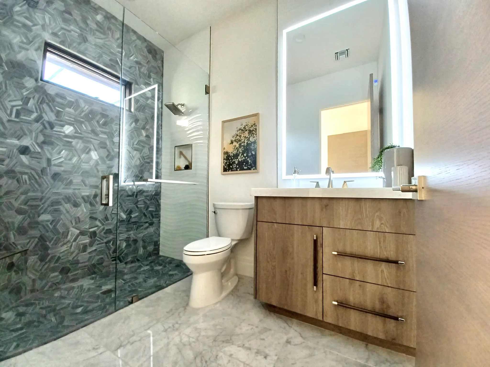 Frameless Glass Shower and LED Mirror | Clear Cut Glass and Tint Modern bathroom with frameless glass shower enclosure, textured tile walls, and backlit LED vanity mirror installed by Clear Cut Glass and Tint in Arizona