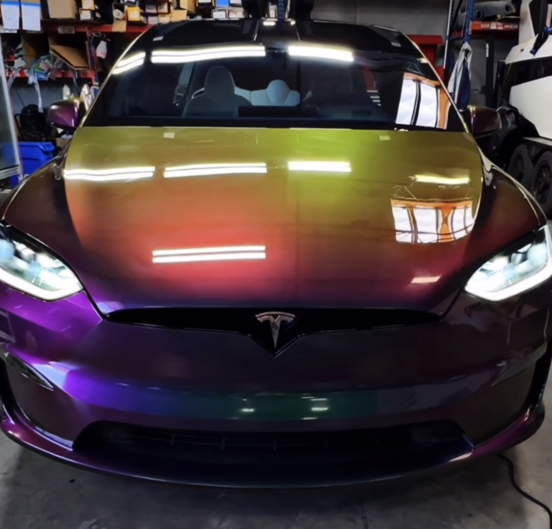Front view of a Tesla Model X wrapped in chameleon color paint protection film inside the Clear Cut Glass and Tint shop, showing dramatic green-to-purple color shift on the hood