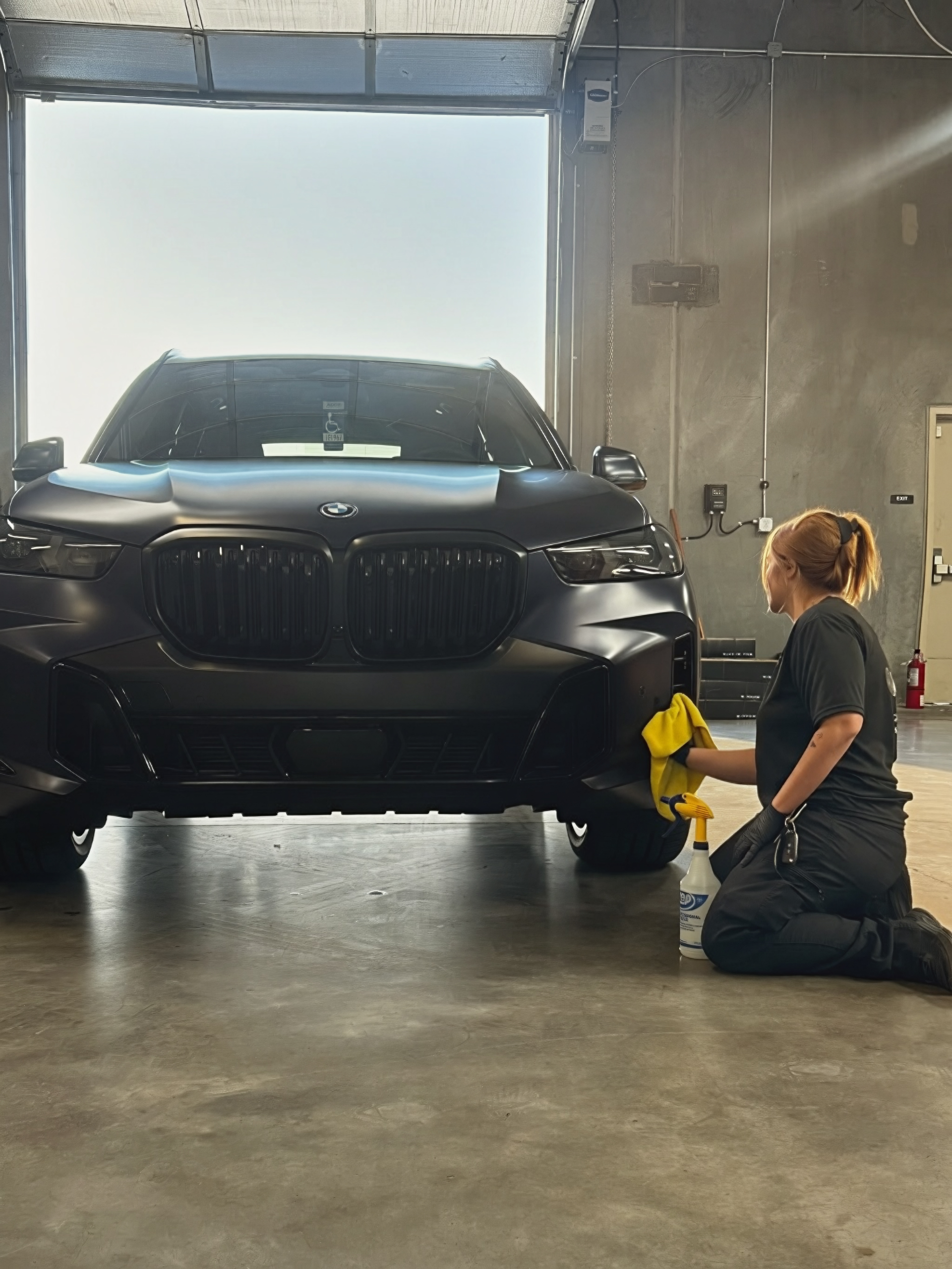 BMW Ceramic Coating Installation | Clear Cut Glass and Tint Glendale AZ Technician applying ceramic coating to matte black BMW inside Clear Cut Glass and Tint shop in Glendale Arizona