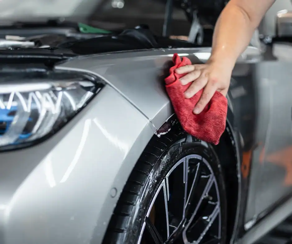 Hand cleaning a car with a microfiber cloth showing proper maintenance to extend paint protection film lifespan
