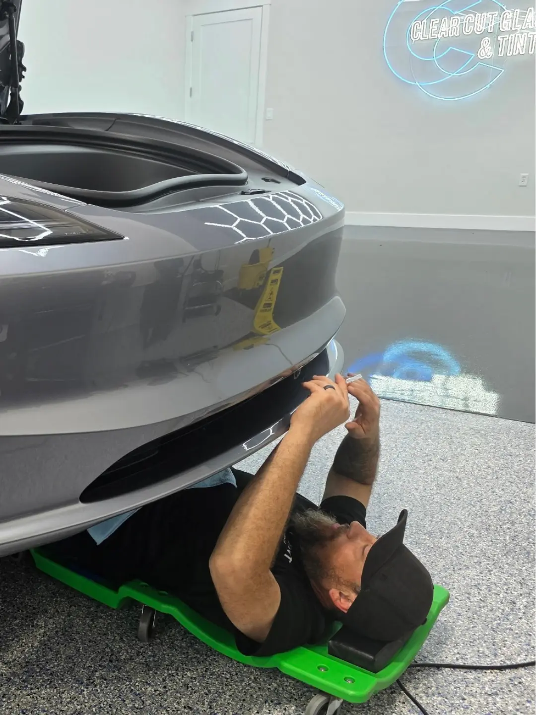 PPF installer hand-finishing paint protection film around a Tesla front bumper opening at Clear Cut Glass & Tint