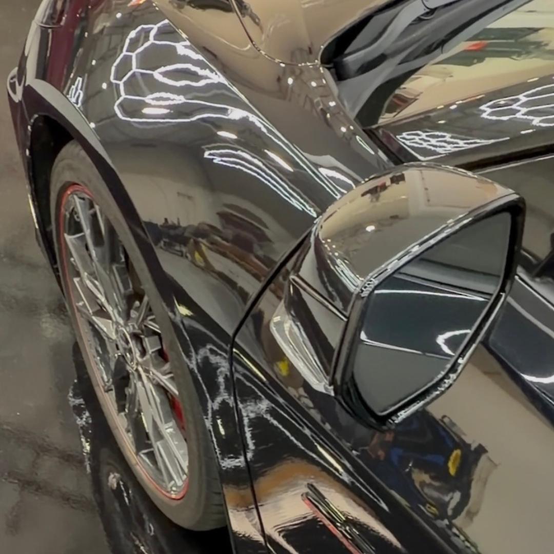Close-up of a black Chevrolet Corvette's side mirror and front fender reflecting overhead lights after ceramic coating.