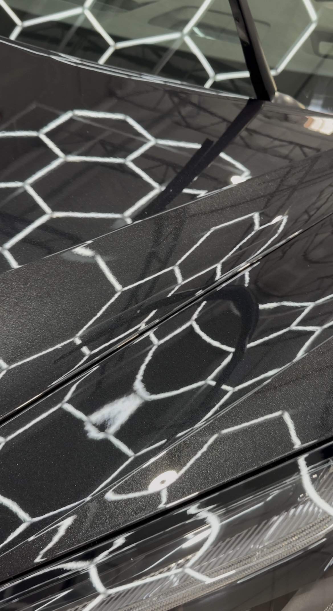 Close-up of glossy black Chevrolet Corvette body panels reflecting hexagonal shop lights after XPEL ceramic coating.