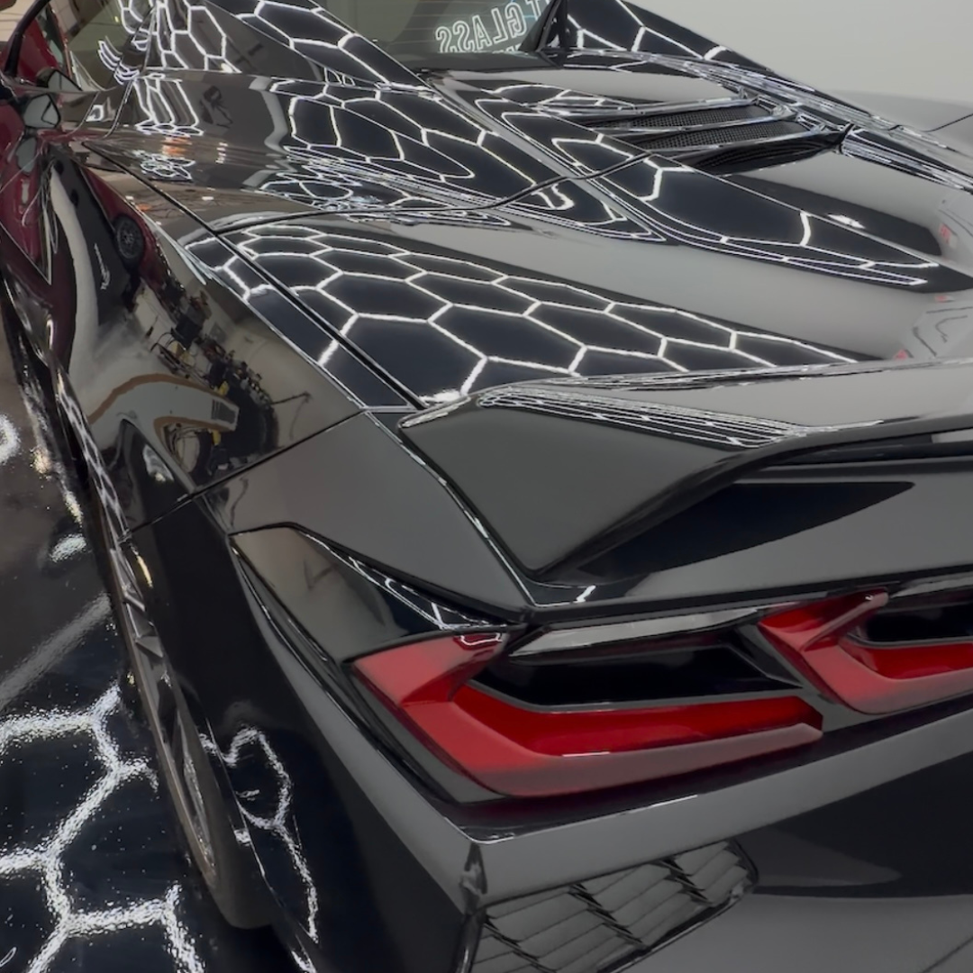 Black Corvette | XPEL Ceramic Coating Rear View Rear three-quarter view of a black Chevrolet Corvette with glossy paint reflecting hexagonal shop lights.