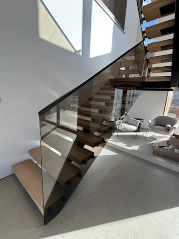 Custom glass railing panels installed along a modern residential staircase with floating wood steps by Clear Cut Glass & Tint.
